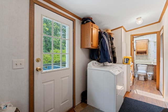 laundry area with light hardwood / wood-style floors, ornamental molding, washing machine and dryer, and cabinets