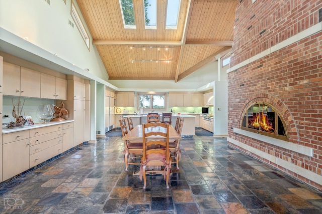 kitchen with a brick fireplace, dark tile flooring, a skylight, high vaulted ceiling, and wooden ceiling