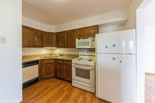 kitchen featuring decorative backsplash, white appliances, light wood-type flooring, and a sink