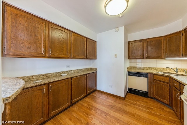 kitchen featuring light stone counters, decorative backsplash, a sink, light wood-style floors, and dishwasher