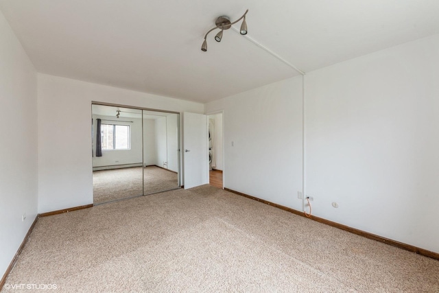 unfurnished bedroom featuring a closet, baseboard heating, carpet, and baseboards