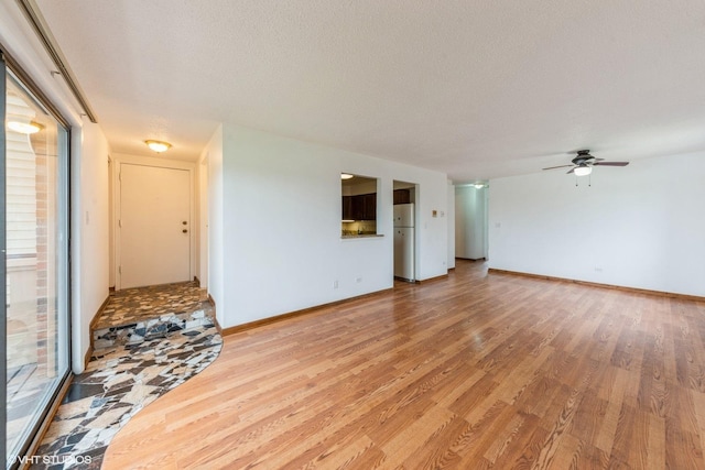 unfurnished living room with baseboards, light wood-type flooring, and a ceiling fan