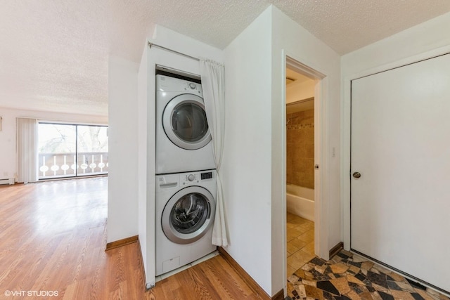 laundry area with stacked washing maching and dryer, a textured ceiling, and light wood-style floors