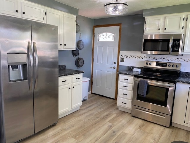 kitchen with white cabinets, backsplash, dark stone counters, stainless steel appliances, and light hardwood / wood-style flooring