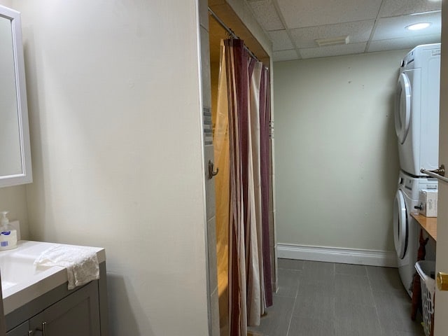 bathroom with a drop ceiling, stacked washer / dryer, vanity, and tile flooring