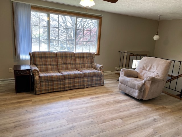 living room with ceiling fan, a textured ceiling, and light wood-type flooring