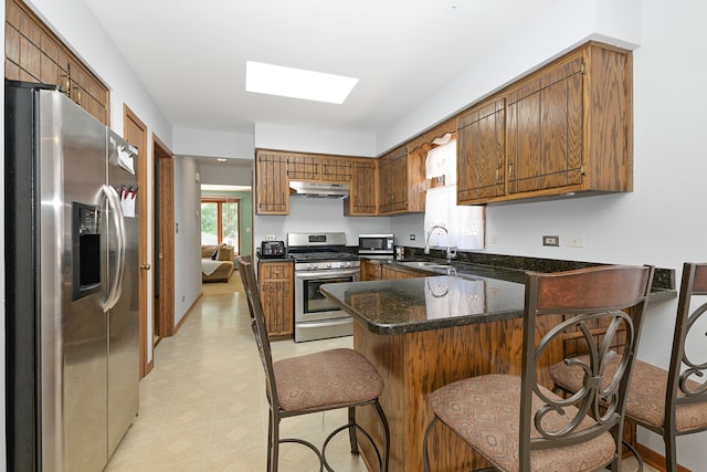 kitchen featuring dark stone countertops, stainless steel appliances, sink, kitchen peninsula, and a breakfast bar