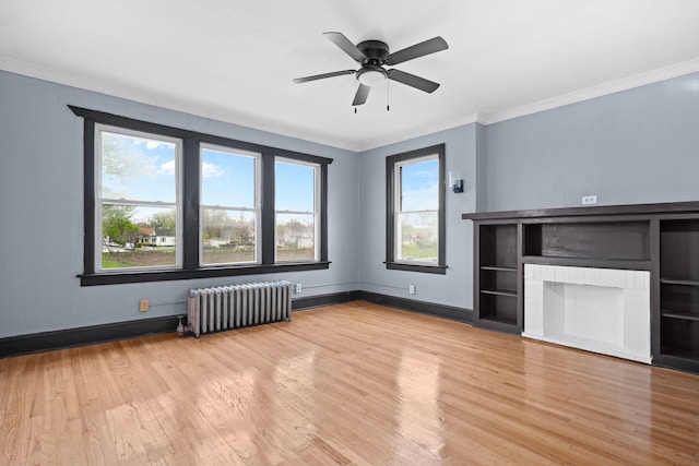 unfurnished living room featuring ceiling fan, a brick fireplace, radiator heating unit, light hardwood / wood-style floors, and crown molding