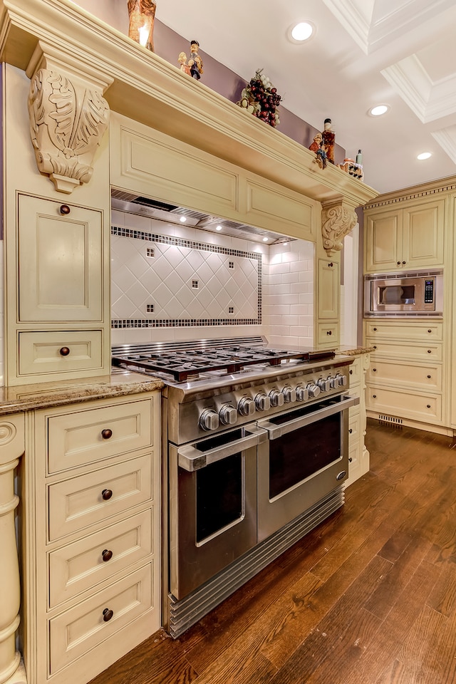 kitchen featuring light stone countertops, cream cabinets, appliances with stainless steel finishes, backsplash, and dark hardwood / wood-style flooring