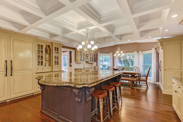 kitchen featuring coffered ceiling, decorative light fixtures, an inviting chandelier, a center island with sink, and a breakfast bar area