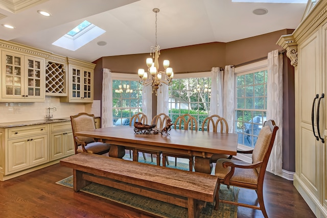 dining room with an inviting chandelier, vaulted ceiling with skylight, dark wood-type flooring, and a healthy amount of sunlight