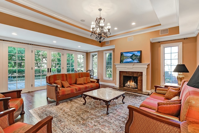 living room with a high end fireplace, french doors, dark hardwood / wood-style flooring, a tray ceiling, and an inviting chandelier