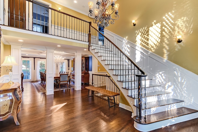 staircase featuring an inviting chandelier, dark hardwood / wood-style flooring, crown molding, and decorative columns