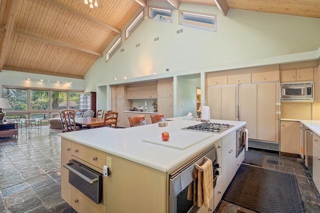 kitchen featuring dark tile floors, built in appliances, high vaulted ceiling, and a center island with sink