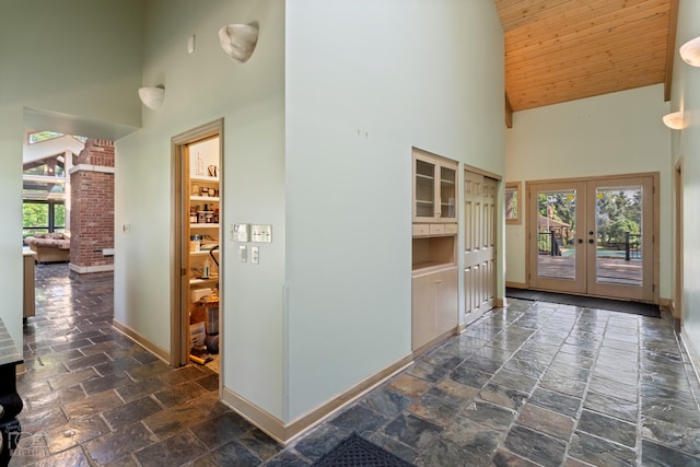 hall with high vaulted ceiling, brick wall, wooden ceiling, french doors, and dark tile floors