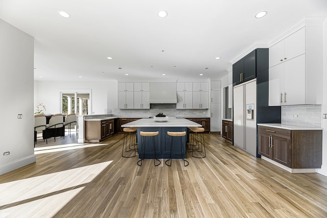 kitchen with a breakfast bar, dark brown cabinets, a center island, light wood-type flooring, and decorative backsplash