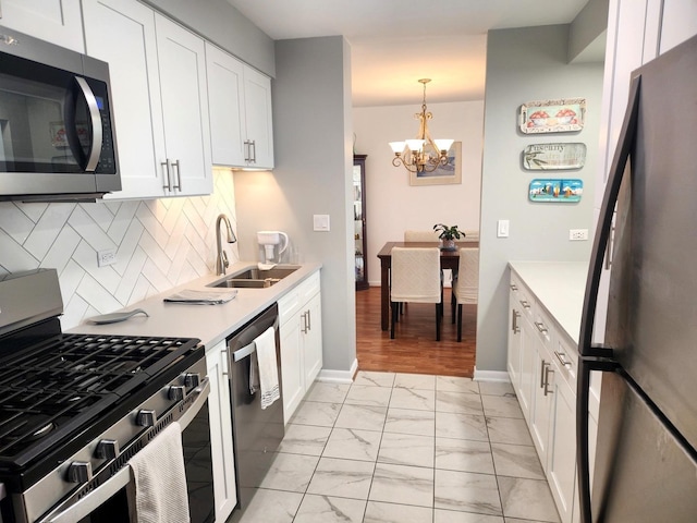 kitchen with a notable chandelier, appliances with stainless steel finishes, a sink, marble finish floor, and backsplash