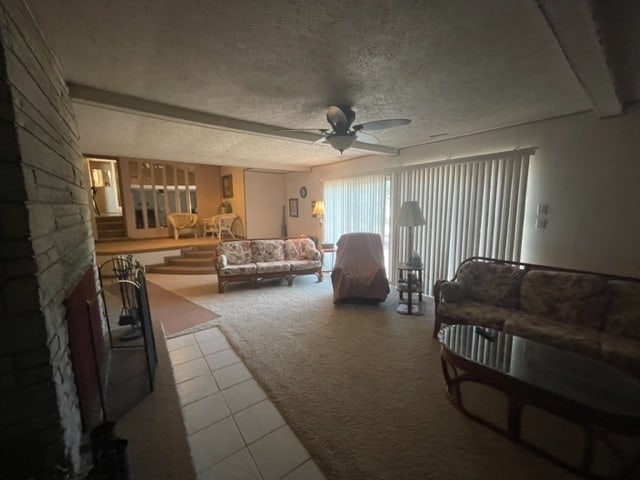 living room featuring light colored carpet, ceiling fan, a textured ceiling, and a fireplace