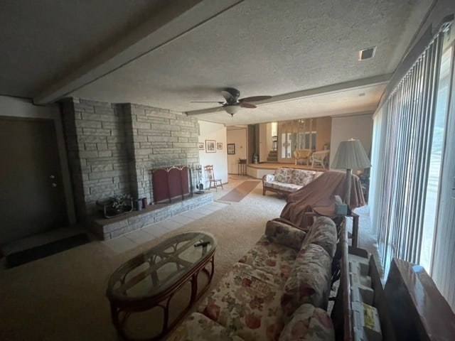 living room with light carpet, a textured ceiling, ceiling fan, and a wood stove