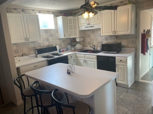 kitchen featuring black dishwasher, a breakfast bar area, white cabinetry, white range with gas cooktop, and ceiling fan