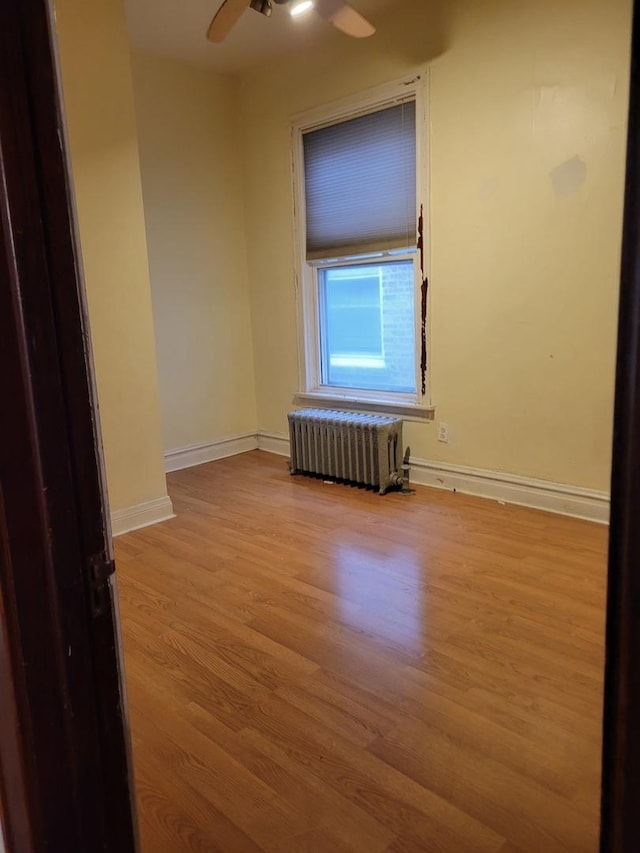 spare room with baseboards, ceiling fan, light wood-style floors, and radiator