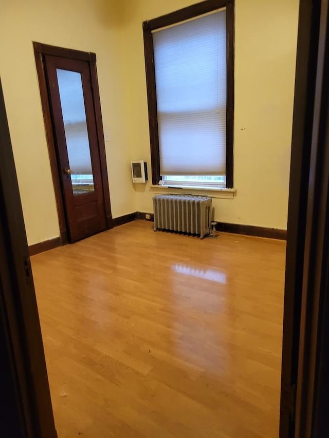 unfurnished room featuring radiator, heating unit, light wood-type flooring, and baseboards