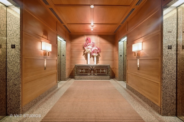 corridor with wood walls, coffered ceiling, wooden ceiling, and light colored carpet