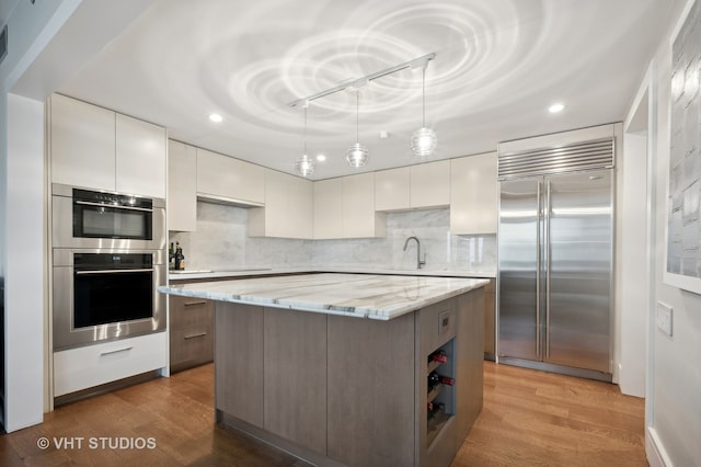 kitchen featuring appliances with stainless steel finishes, light hardwood / wood-style flooring, tasteful backsplash, white cabinetry, and a center island