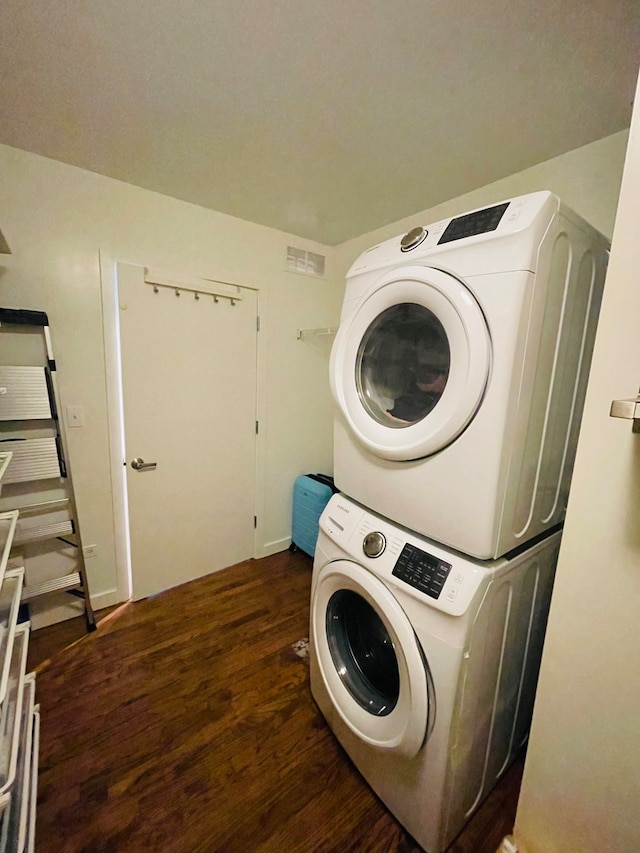 laundry room featuring stacked washer / dryer and dark wood-type flooring