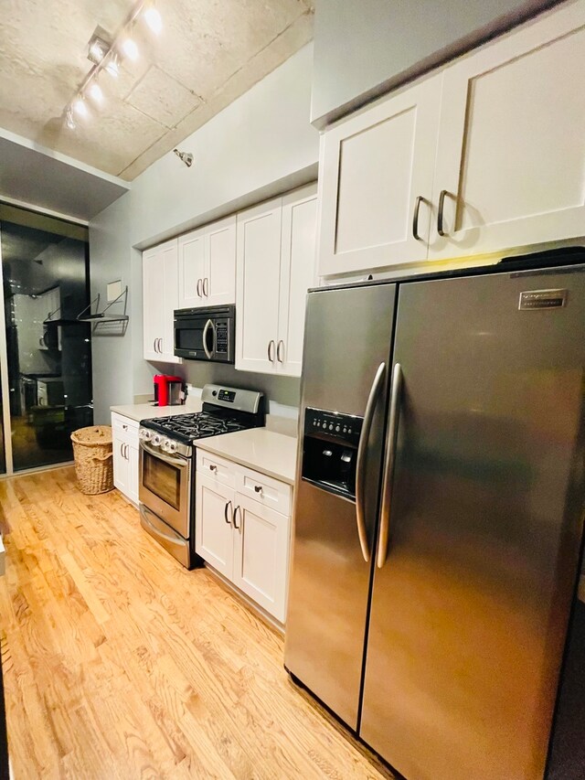 kitchen featuring white cabinets, rail lighting, light hardwood / wood-style flooring, and stainless steel appliances