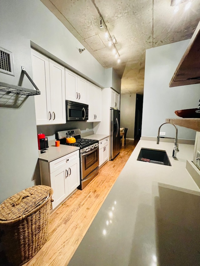 kitchen with sink, white cabinets, light hardwood / wood-style flooring, stainless steel appliances, and track lighting