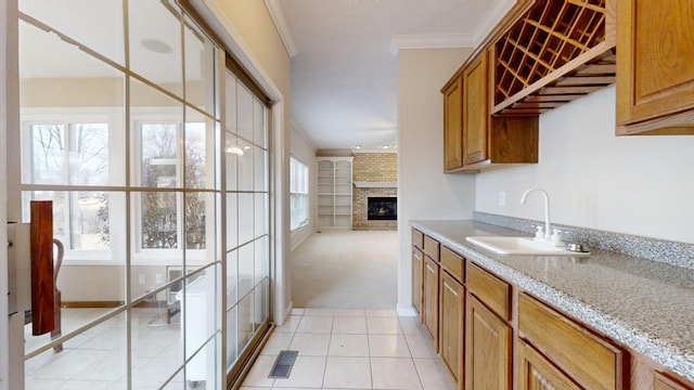 kitchen with brick wall, sink, light tile floors, a fireplace, and light stone countertops