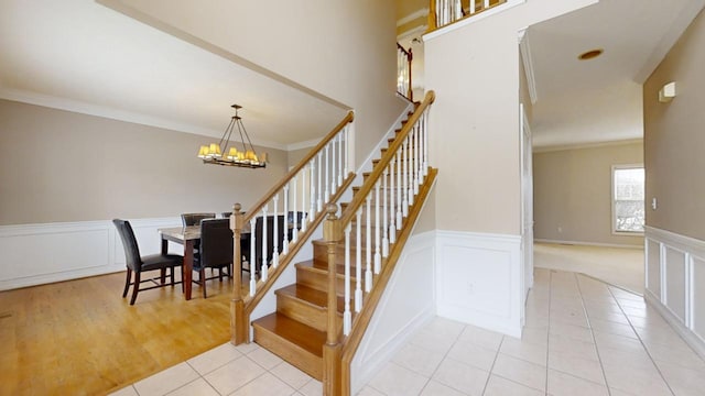 stairs with an inviting chandelier, crown molding, and light tile floors