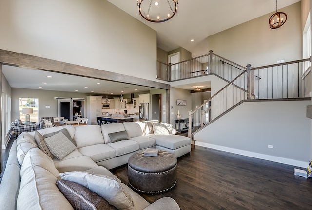 living room with a notable chandelier, dark wood-type flooring, and a towering ceiling