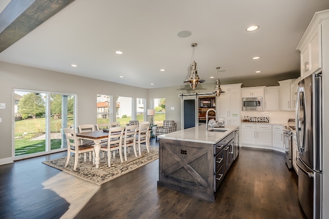 kitchen featuring an island with sink, pendant lighting, light stone countertops, appliances with stainless steel finishes, and dark hardwood / wood-style flooring