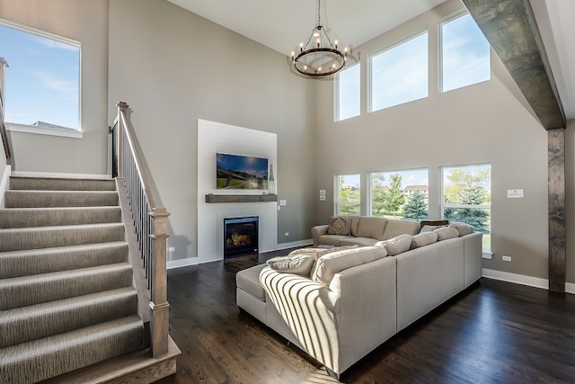 living room with a large fireplace, a notable chandelier, dark wood-type flooring, and a towering ceiling