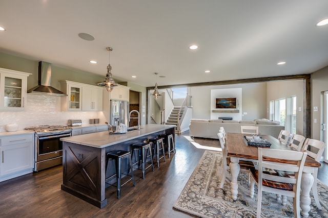 kitchen featuring dark hardwood / wood-style flooring, a center island with sink, stainless steel appliances, pendant lighting, and wall chimney range hood