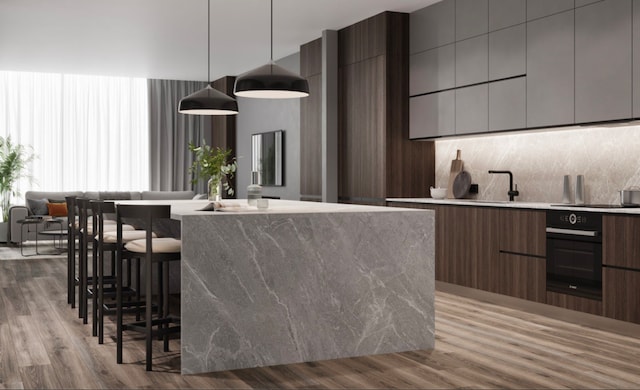 kitchen with light hardwood / wood-style floors, oven, hanging light fixtures, and a kitchen bar