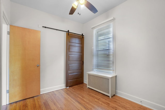 interior space with a barn door, ceiling fan, radiator, and light wood-type flooring