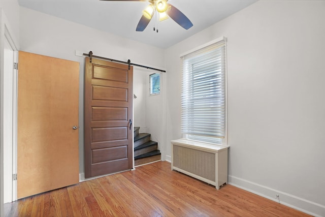 foyer entrance featuring a barn door, ceiling fan, radiator heating unit, and light hardwood / wood-style floors