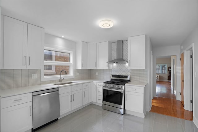 kitchen with appliances with stainless steel finishes, sink, light tile floors, white cabinets, and wall chimney range hood