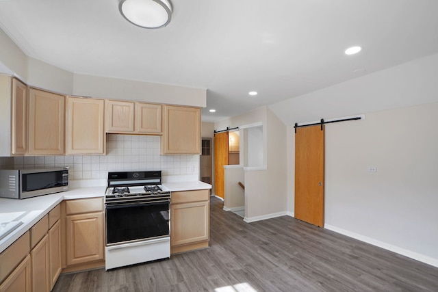 kitchen featuring light brown cabinets, range, a barn door, hardwood / wood-style floors, and backsplash