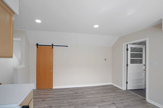 empty room featuring a barn door, lofted ceiling, and light hardwood / wood-style flooring