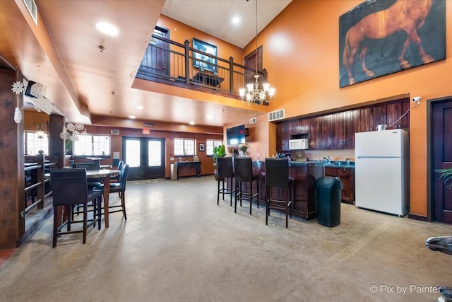 interior space with white appliances, a notable chandelier, a kitchen breakfast bar, a towering ceiling, and french doors