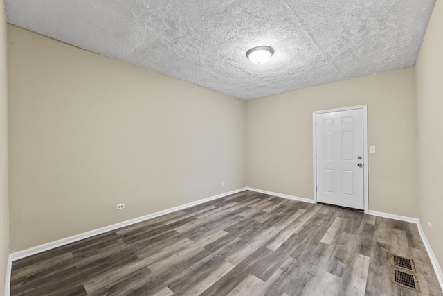 unfurnished room with a textured ceiling, wood finished floors, visible vents, and baseboards