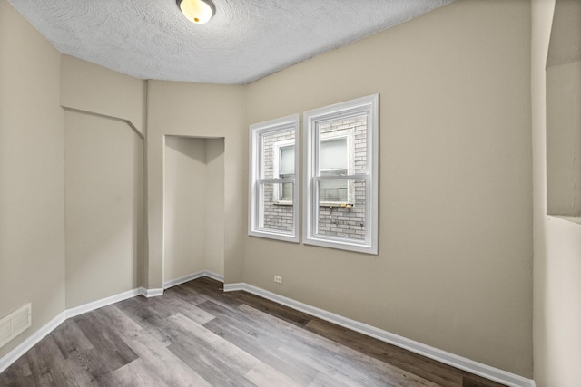 unfurnished room featuring visible vents, a textured ceiling, baseboards, and wood finished floors