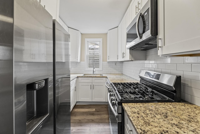 kitchen featuring dark wood finished floors, stainless steel appliances, tasteful backsplash, a sink, and light stone countertops