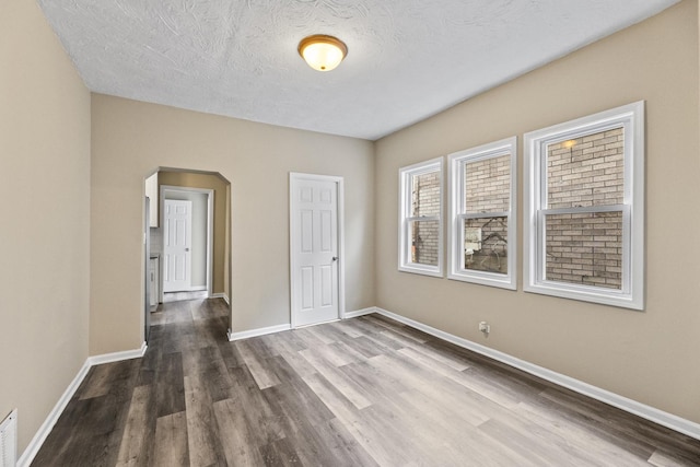unfurnished room featuring dark wood-style floors, a textured ceiling, arched walkways, and baseboards