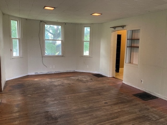 empty room with built in shelves and dark hardwood / wood-style floors