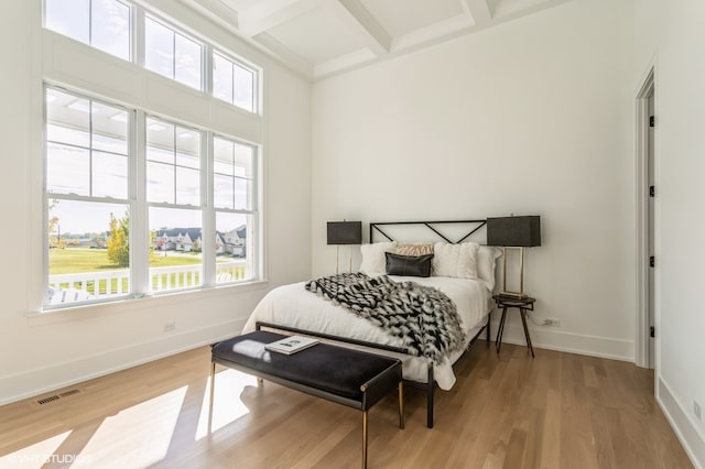 bedroom with multiple windows, coffered ceiling, light hardwood / wood-style flooring, and beam ceiling